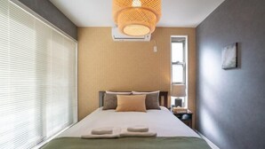 Una habitación de hotel moderna con cama, mesita de noche, lámpara y un amplio ventanal con persianas.