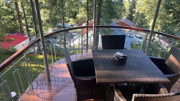 Un balcon doté de meubles en osier et d’une table, offrant une vue sur une zone boisée avec des maisons en arrière-plan.