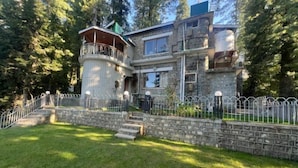 Une maison en pierre à deux étages, dotée d’un balcon, d’un escalier en pierre et d’une cour clôturée.