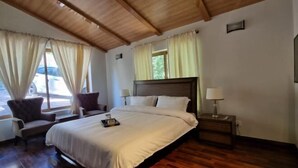 Une chambre avec un plafond en bois, un grand lit avec une literie blanche, deux tables de chevet avec des lampes et une fenêtre avec des rideaux.