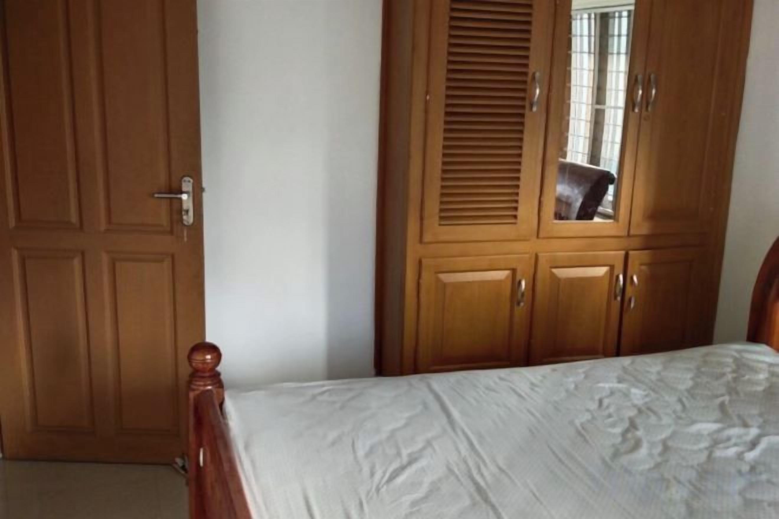 A bedroom with a wooden wardrobe, a bed with a white bedspread, and a door with a handle.