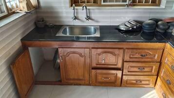 Una cocina con encimera negra, armarios de madera, un lavamanos de acero inoxidable y una ventana con diseño de cuadrícula.