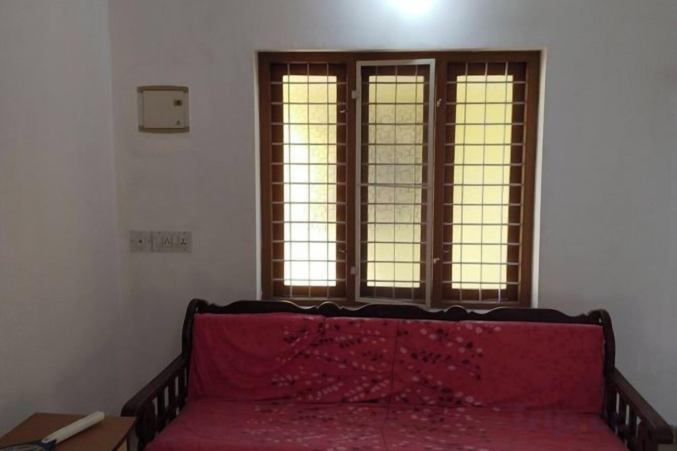 A room with a bed, a window with bars, a wall socket, and a light switch.