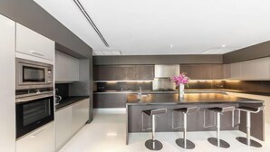 A modern kitchen with a central island, bar stools, and stainless steel appliances. - Baan Santisuk (Phuket)