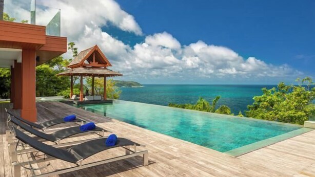A modern infinity pool with clear blue water, lounge chairs, and a wooden deck. - Baan Santisuk (Phuket)