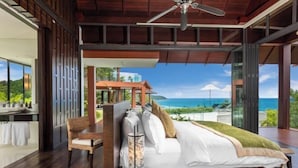 A bedroom with a large bed, a chair, and a view of the ocean. - Baan Santisuk (Phuket)