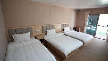 A hotel room with three beds, wooden flooring, and a view of the outdoors.