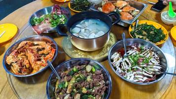 A round table with various dishes, including seafood, vegetables, and a pot of boiling water.
