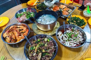 Una mesa redonda con diversos platos, entre ellos mariscos, verduras y una olla con agua hirviendo.