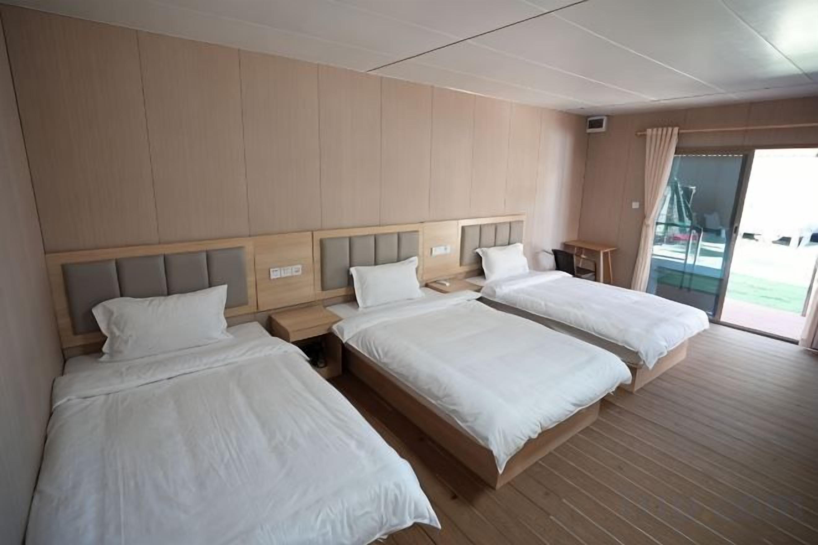 Habitación de hotel con tres camas, suelo de madera y vistas al exterior.