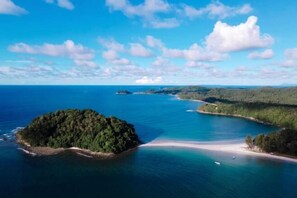 An aerial view of a coastal area with a small island surrounded by clear blue waters and a sandy beach. - STARHOUSE (Kudat Division)