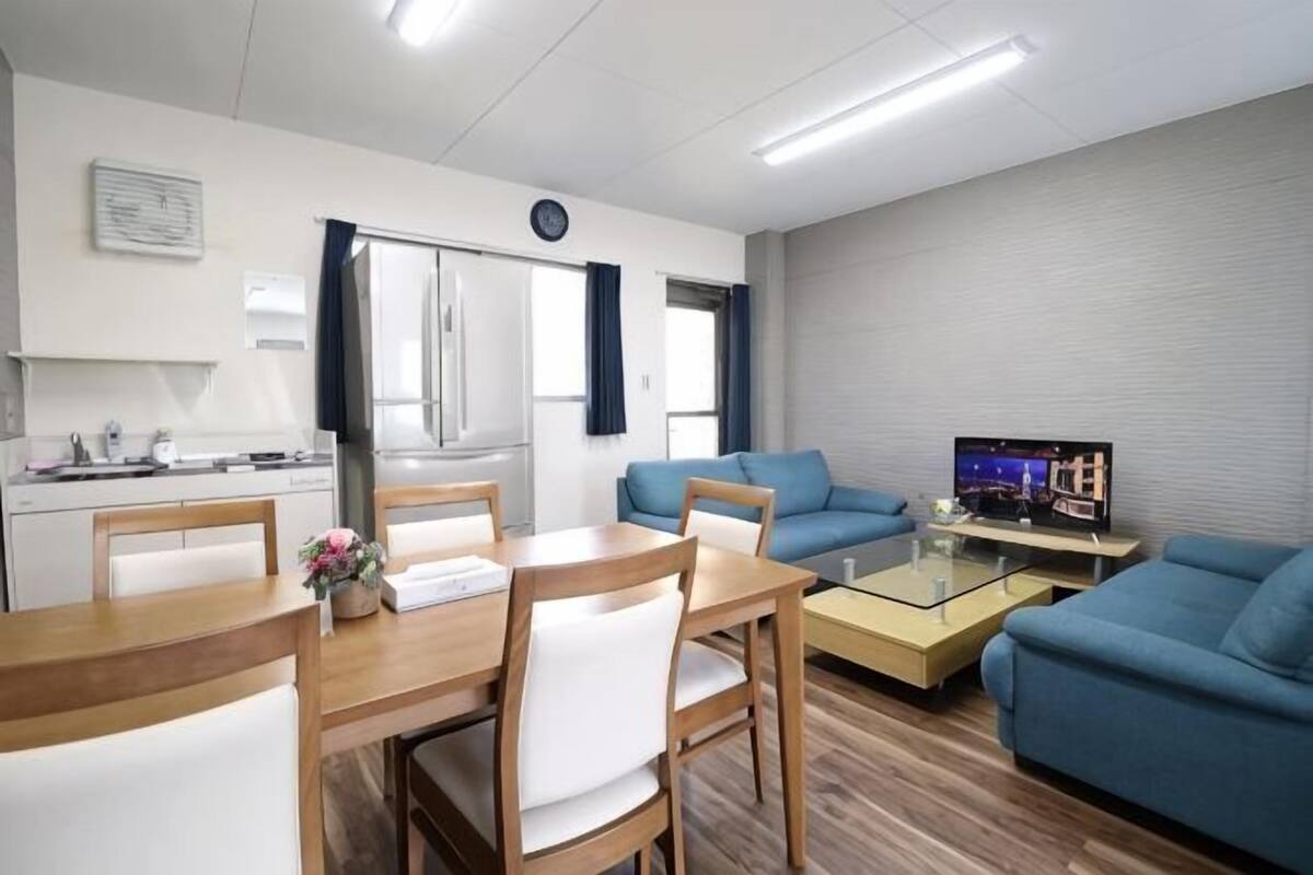 Un espacio habitable compacto con comedor, sofá, televisor y kitchenette.