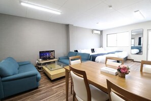 Ein Hotelzimmer mit einem Bett, einer Couch, einem Esstisch, einem Fernseher und einem Spiegel.