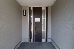 Ein schmaler Korridor mit einer dunklen Tür, einem gerahmten Aushang und einem Lichtschalter an der Wand.