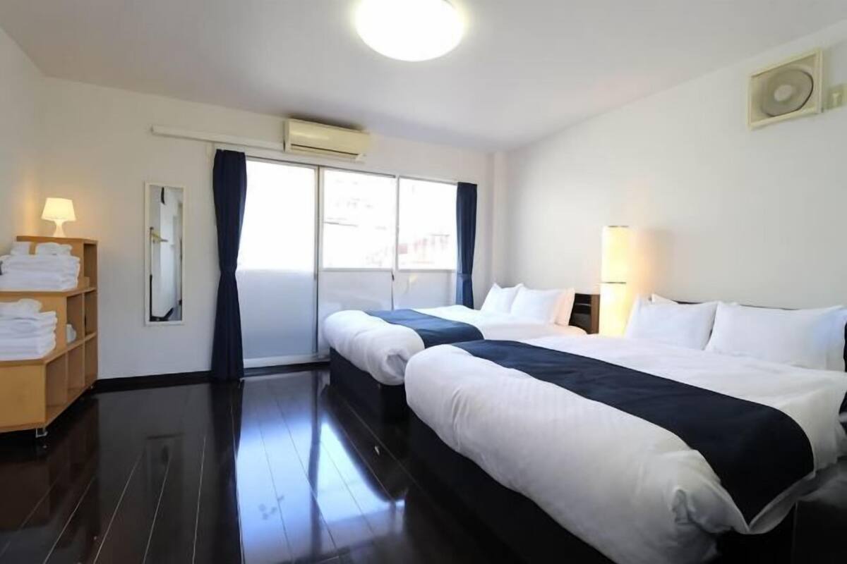 Une chambre d’hôtel avec deux lits, une fenêtre avec des rideaux, une lampe de chevet, un miroir et une étagère avec des serviettes pliées.