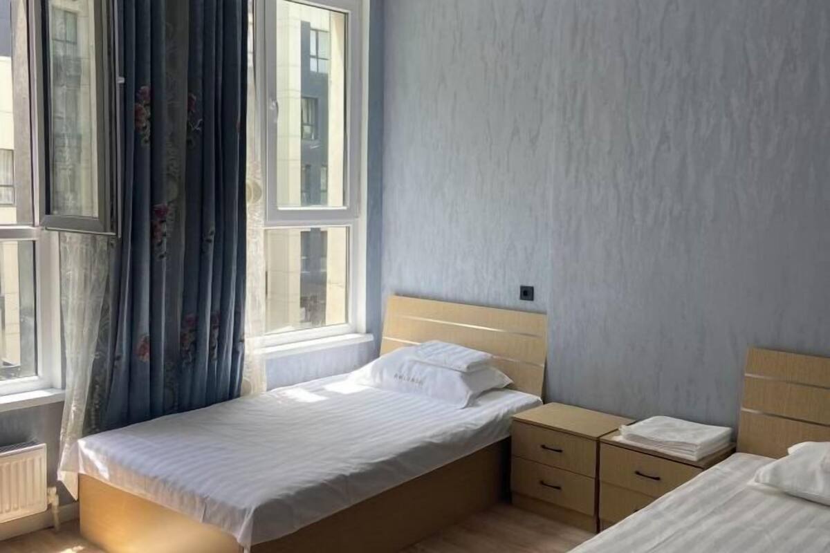 Un dormitorio con una cama individual, una mesita de noche, un aparador y una ventana con cortinas.