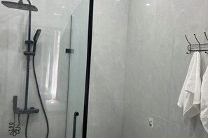 Een moderne badkamer met een douchecabine van glas, een handdoekrek met een witte handdoek en een zichtbare elektriciteitsdop aan de muur.