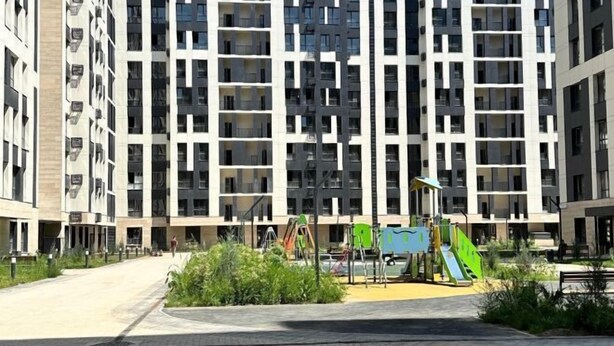 A modern apartment building with multiple balconies and a playground area with slides and swings. - Ali Boutique Guesthouse (Almaty)