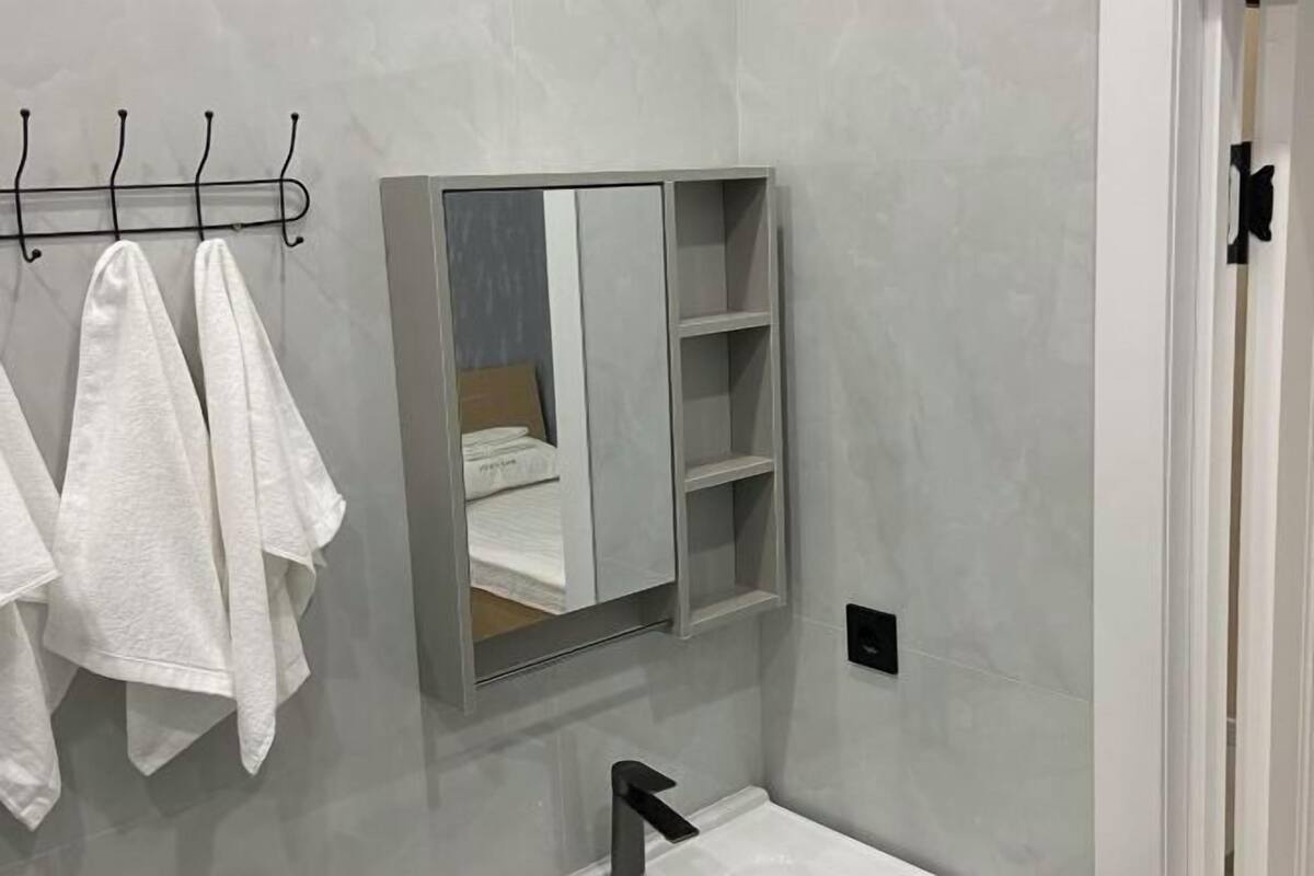 Un baño con espejo, toallero con toallas, lavamanos y una puerta.