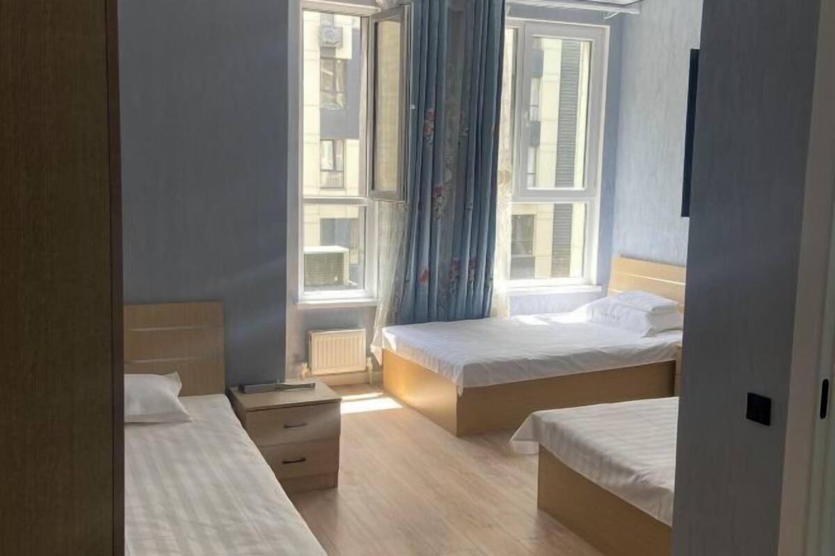 Un dormitorio con dos camas, una ventana con cortinas, un radiador y suelo de madera.