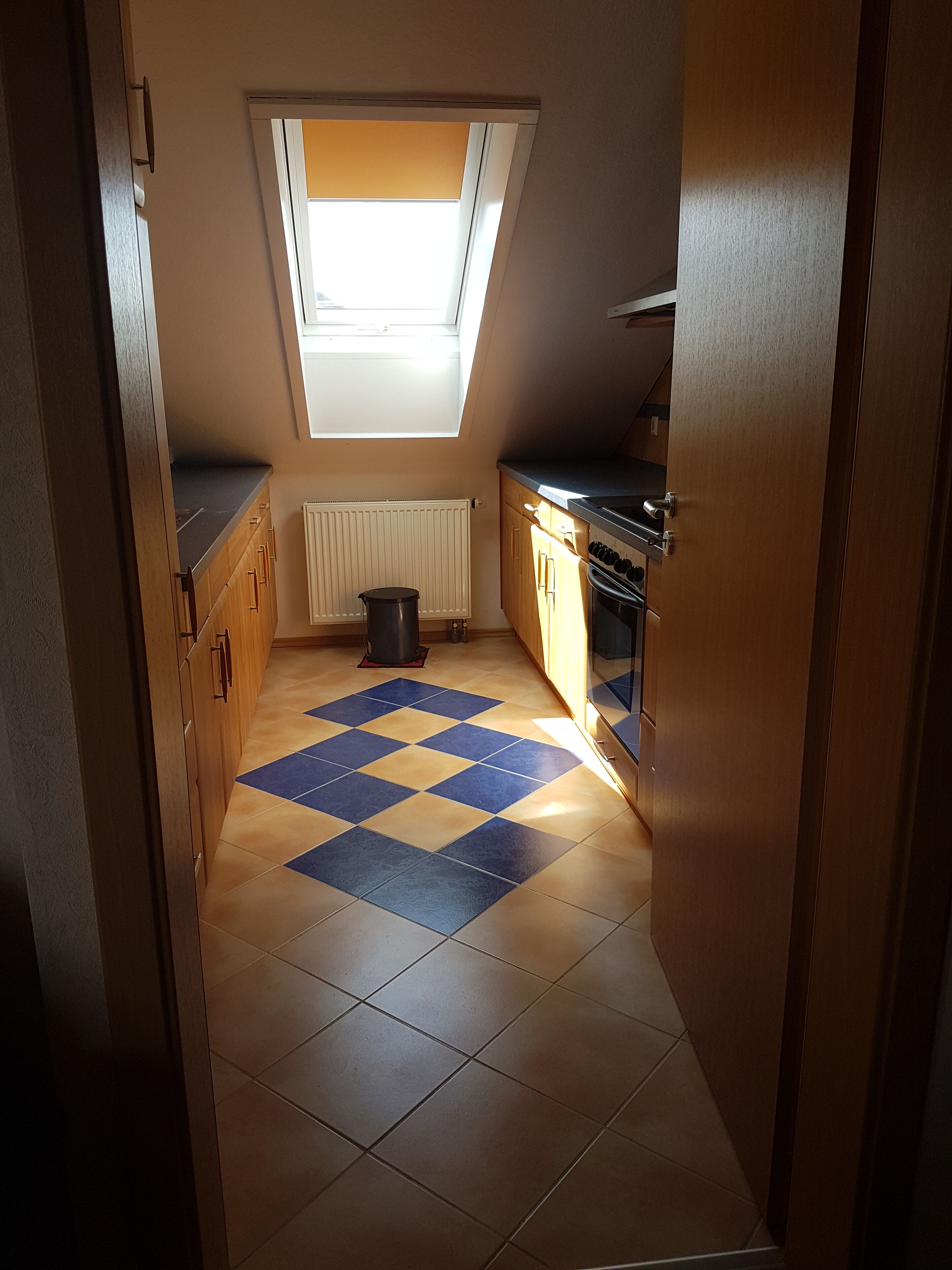 A kitchen with a skylight, wooden cabinets, a tiled floor, and a stove.