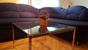 Un saló amb una taula de centre de vidre, una cistella de vimet amb flors i un sofà de color fosc.