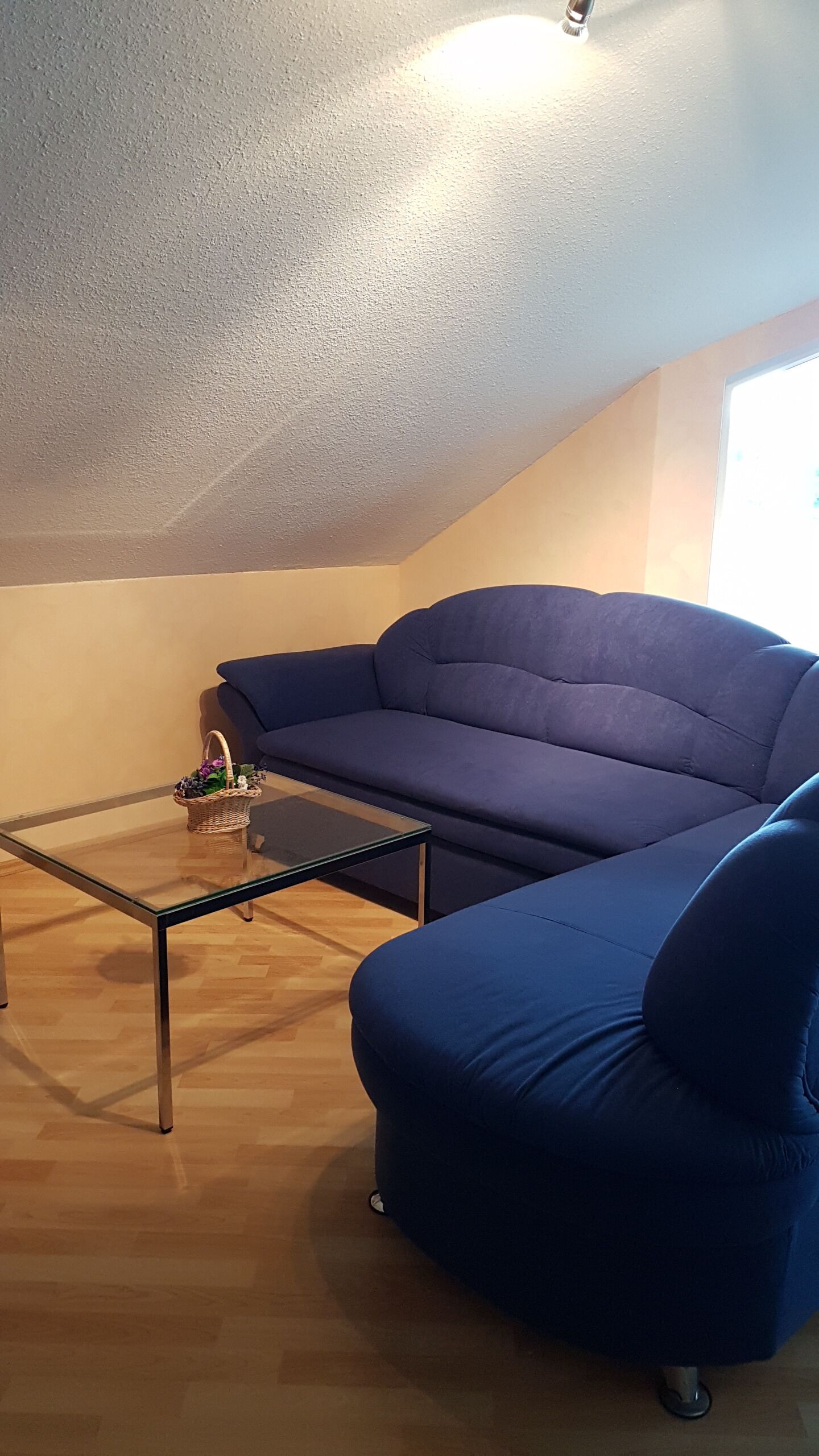 A cozy living room with a blue sofa, a glass coffee table, and a wicker basket on a wooden floor.