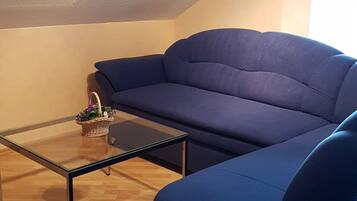 A cozy living room with a blue sofa, a glass coffee table, and a wicker basket on a wooden floor.