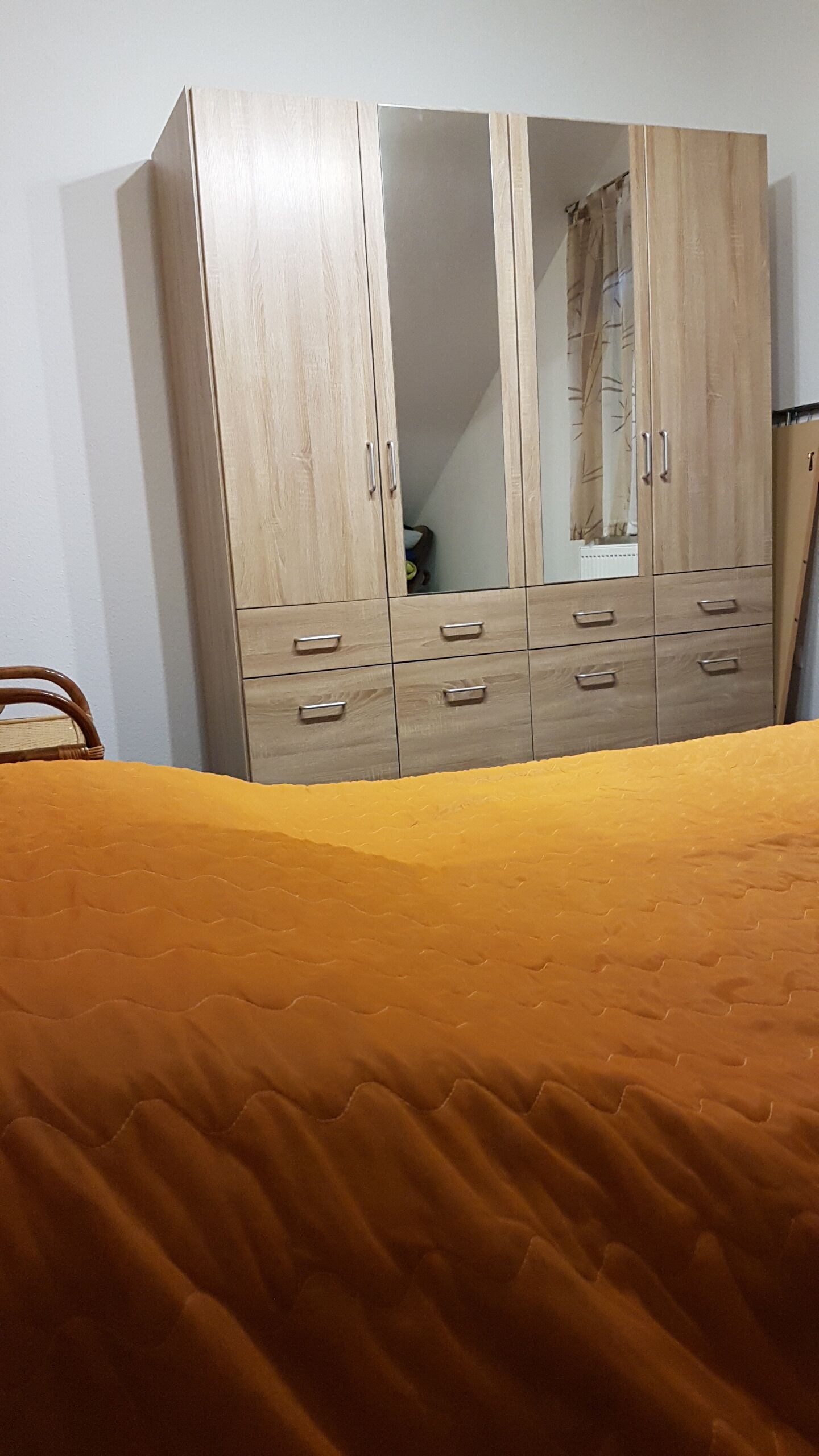 Une chambre à coucher avec un lit, une armoire en bois dotée de nombreux tiroirs et un miroir.