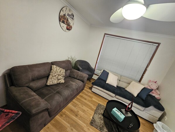 A living room with a brown sofa, a grey sofa, a small black table, and a ceiling fan.
