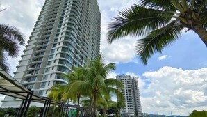 A tall building with a curved facade, surrounded by palm trees and a body of water. - 3806 Macrolink 6pax Cozy Legoland Netflix BySTAY (Iskandar Puteri)