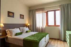 A double bed with a green throw, two bedside tables with lamps, a window with curtains, and a small green cabinet. - Luxury Villa Suzana (Hersonissos)