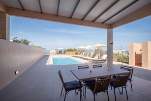 An outdoor patio with a pool, dining table, and chairs, overlooking a pool area with lounge chairs. - Luxury Villa Suzana (Hersonissos)