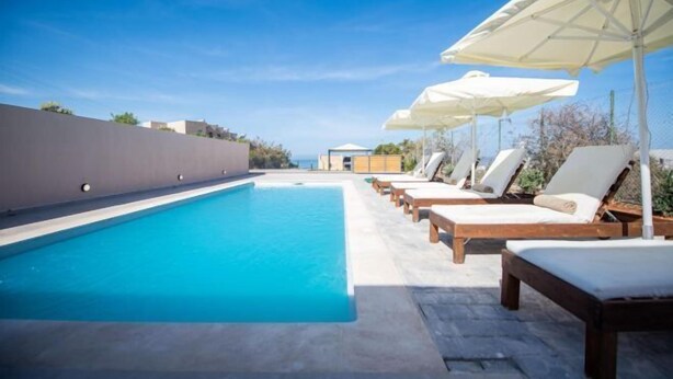 Une piscine avec des chaises longues et des parasols, un ciel dégagé et une vue sur la mer.