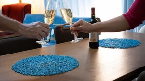 Duas pessoas brindando com taças de champanhe, uma garrafa de vinho e um jogo americano azul tecido sobre uma mesa.