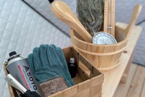 A wooden basket containing a can of Asoto, a green glove, a small bottle, and wooden utensils. - Grace House (Higashiizu)