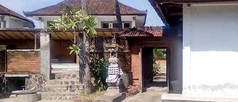 A residential area with a house featuring a tiled roof, a staircase leading to a porch, and a small garden with a palm tree.