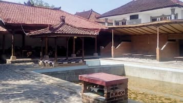A courtyard with a tiled roof structure, a pool, and a stone pathway.