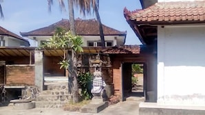 A courtyard with a stone statue, a small garden, and a building with a tiled roof. - Guest House Surya Ayu Permai Buleleng Mitra RedDoorz (Bali)