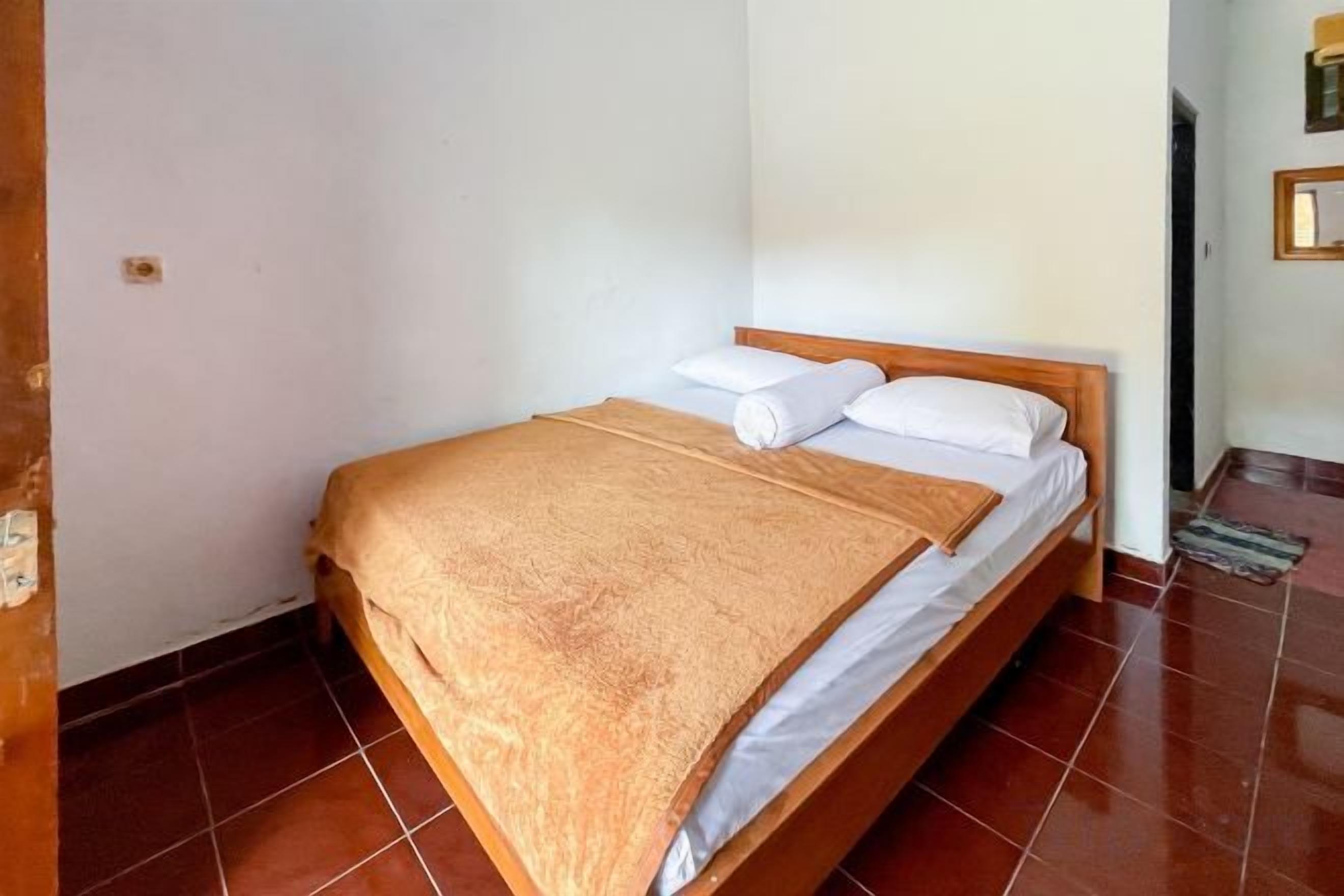 Una cama individual con estructura de madera, sábanas blancas y una manta marrón.