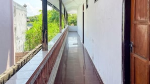 A corridor with a tiled floor, white walls, and a wooden door on the right. - Guest House Surya Ayu Permai Buleleng Mitra RedDoorz (Bali)