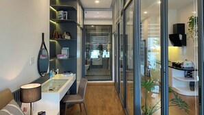 A modern, compact living space with a built-in desk, shelves, and a glass door leading to a kitchen area. - Apartments in District 2-The Sun Avenue (Ho Chi Minh City)