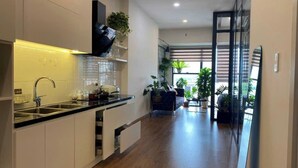A modern kitchen with a black countertop, white cabinets, and a built-in oven. There is a window with blinds and a potted plant on the counter. - Apartments in District 2-The Sun Avenue (Ho Chi Minh City)