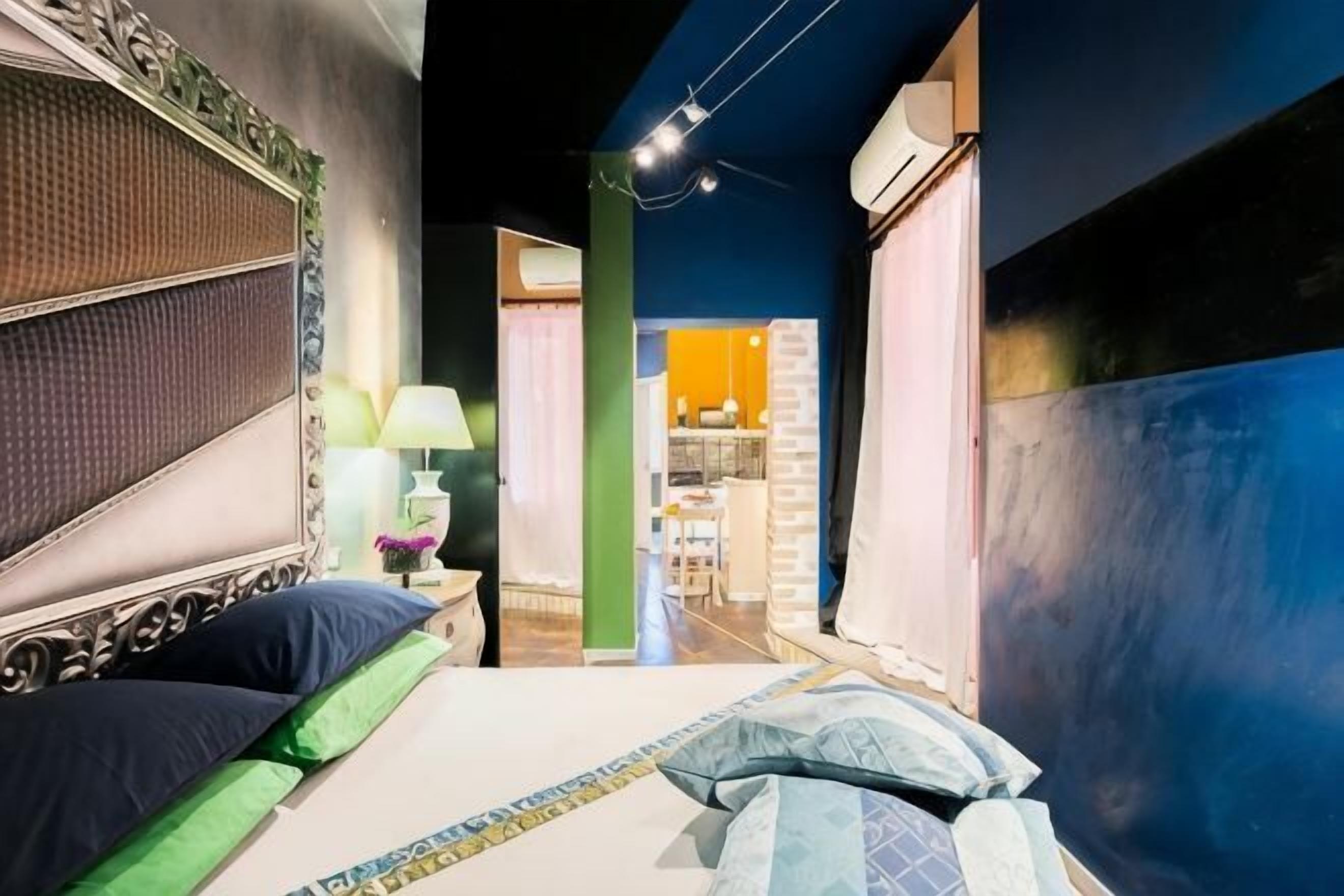 Un corridoio stretto che porta a una camera da letto con un letto, un comodino e una lampada.