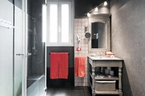 Un bagno con cabina doccia in vetro, un lavabo con specchio e un portascopino.