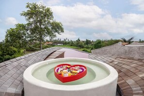 A heart-shaped hot tub with a pool, surrounded by a curved roof structure and greenery. - Clan Living - the Lovers Ubud Private Villas (Bali)