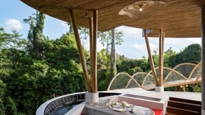 Un área de hidromasaje exterior de lujo con un deck de madera, una zona de estar con cojín rojo y vistas a exuberante vegetación.