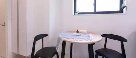A small dining area with a round table and two black chairs, a window with a plant, and a white cabinet.