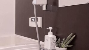 A bathroom with a shower, a white bottle, and a potted plant on a shelf. - japan house sugamo (Tokyo)