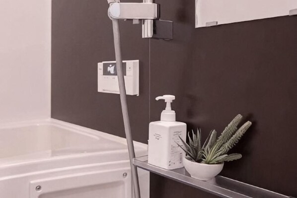 A bathroom with a shower, a white bottle, and a potted plant on a shelf. - japan house sugamo (Tokyo)